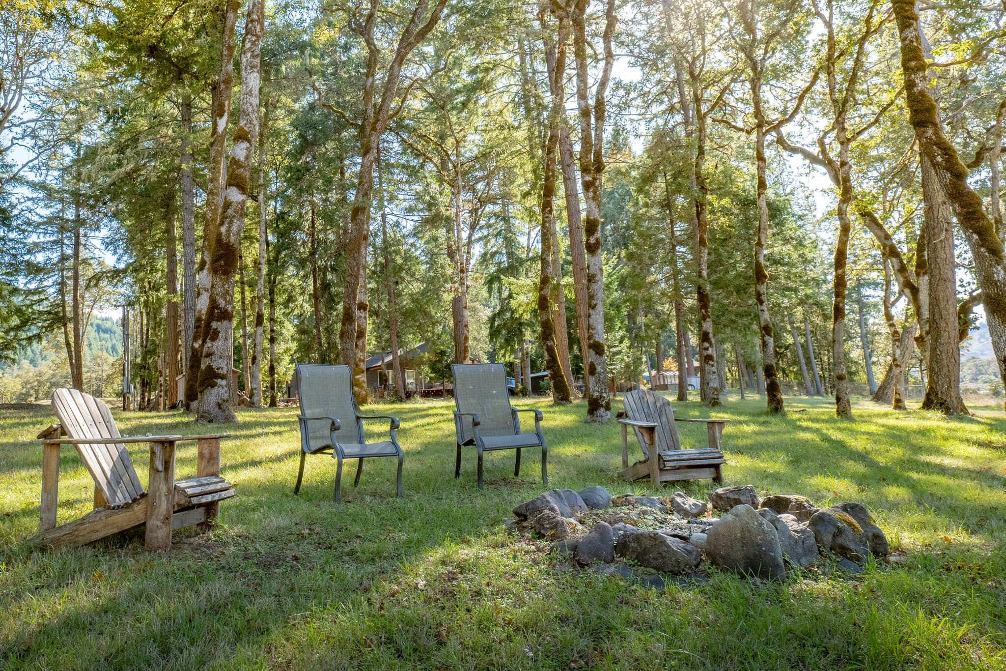 Backyard fire pit with Adirondack chairs among tall trees — real estate photography by Hahn Media, Oregon
